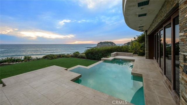 pool at dusk featuring a yard, a water view, and a patio area