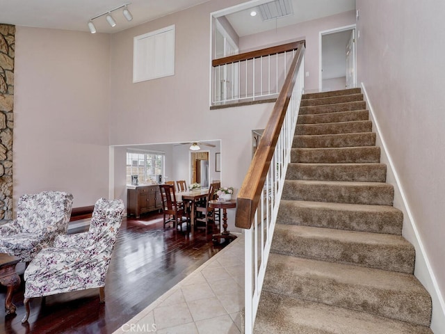 stairs featuring a ceiling fan, rail lighting, wood finished floors, and a towering ceiling