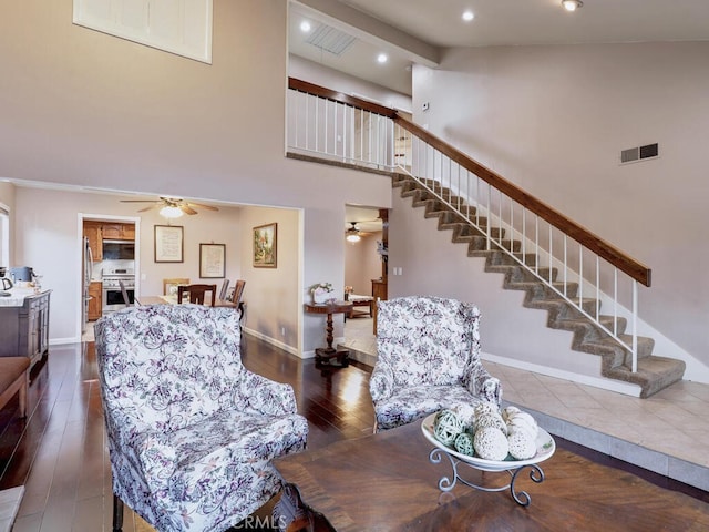 living area featuring stairs, a high ceiling, a ceiling fan, and visible vents