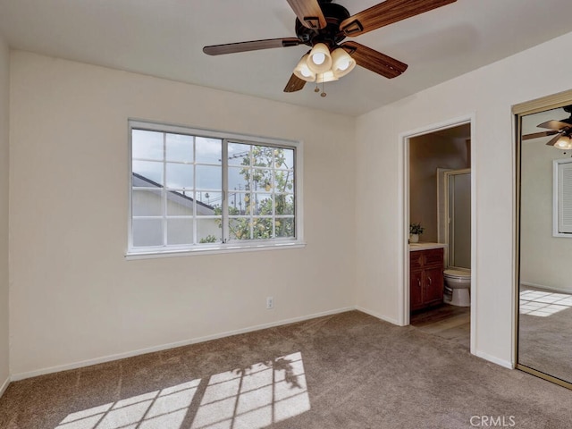 unfurnished bedroom with carpet flooring, baseboards, ensuite bathroom, and ceiling fan