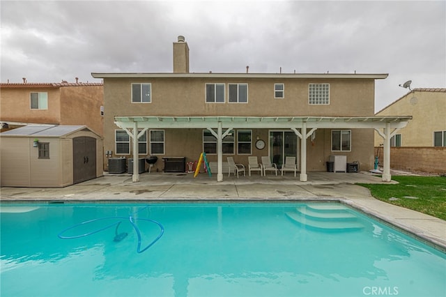 rear view of property featuring a storage unit, an outbuilding, a patio, an outdoor pool, and a chimney