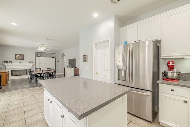 kitchen with a ceiling fan, arched walkways, white cabinets, stainless steel fridge with ice dispenser, and light tile patterned floors