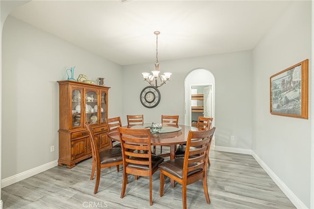 dining space with baseboards, arched walkways, light wood-style floors, and an inviting chandelier