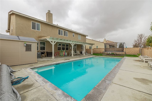 view of pool featuring an outbuilding, a fenced backyard, a patio, and a trampoline