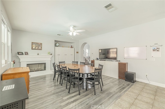 dining room with arched walkways, visible vents, a ceiling fan, and a glass covered fireplace