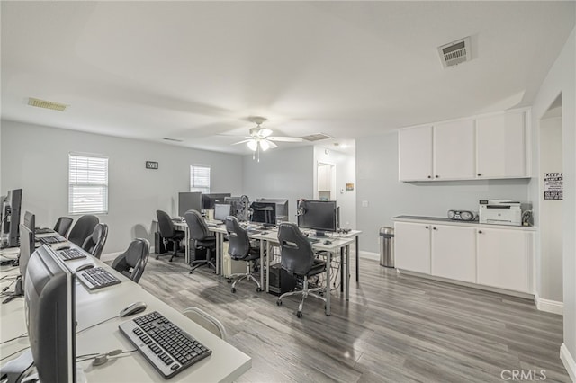 home office with light wood-style floors, a ceiling fan, visible vents, and baseboards