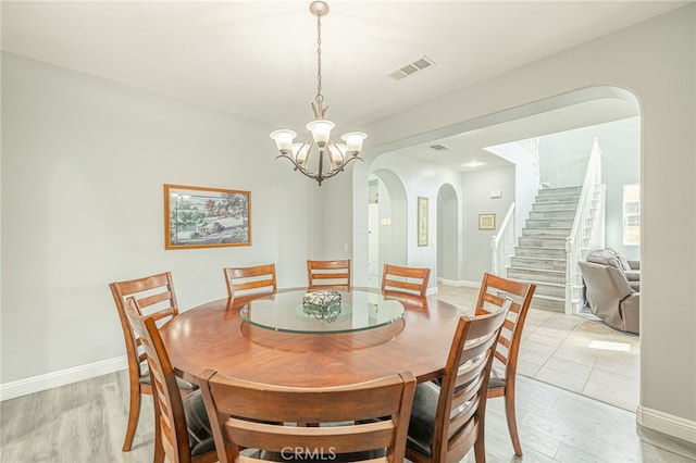 dining area with stairway, visible vents, an inviting chandelier, arched walkways, and light wood-style floors