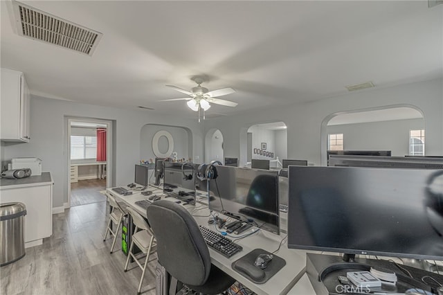 home office with a ceiling fan, baseboards, visible vents, arched walkways, and light wood-type flooring