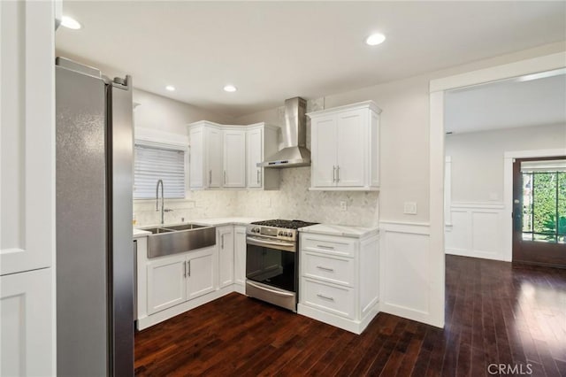 kitchen featuring a wainscoted wall, a sink, dark wood-style floors, appliances with stainless steel finishes, and wall chimney exhaust hood