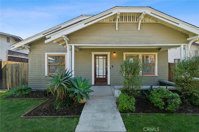 bungalow-style home with covered porch, a front lawn, and fence