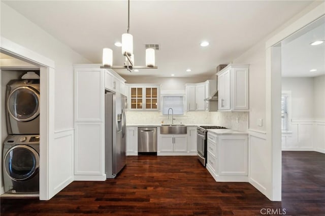 kitchen featuring a sink, light countertops, appliances with stainless steel finishes, stacked washer / drying machine, and dark wood-style flooring