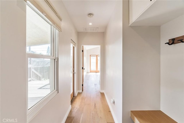 hall with visible vents, baseboards, and light wood finished floors