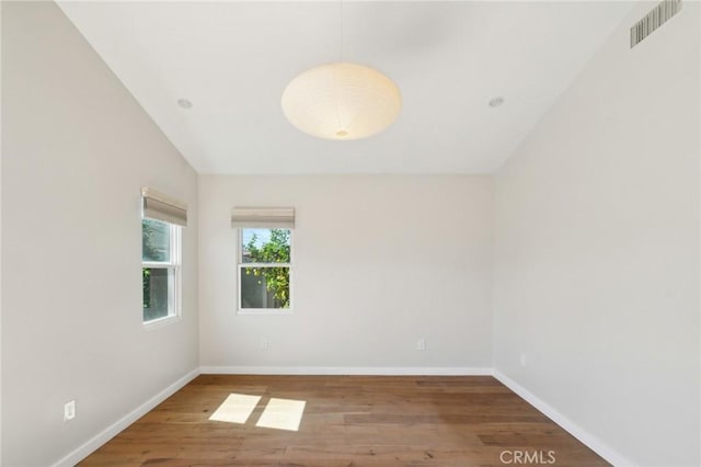 empty room with visible vents, baseboards, lofted ceiling, and wood finished floors