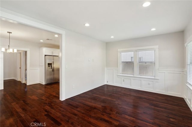 spare room with dark wood-type flooring, a chandelier, recessed lighting, wainscoting, and a decorative wall