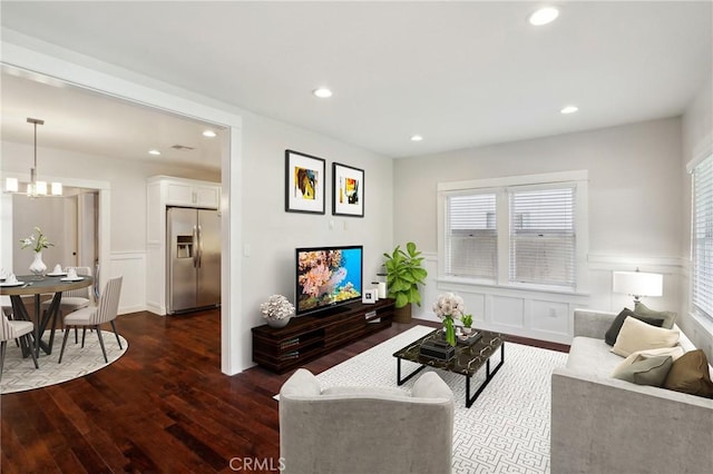 living room featuring an inviting chandelier, recessed lighting, dark wood-type flooring, wainscoting, and a decorative wall