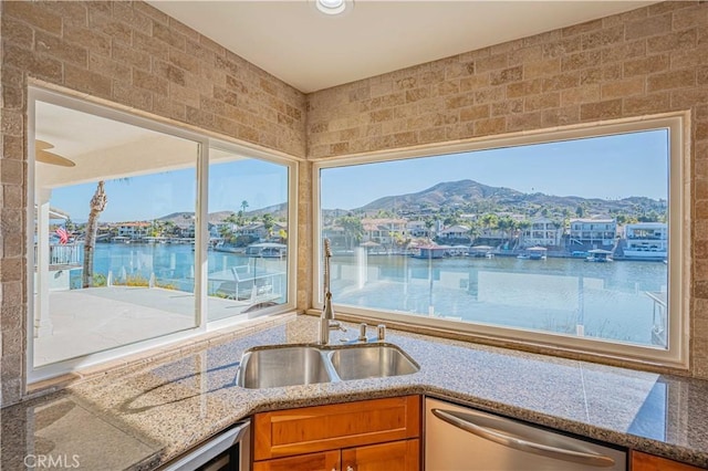 kitchen with brown cabinetry, stone counters, a sink, dishwasher, and a mountain view