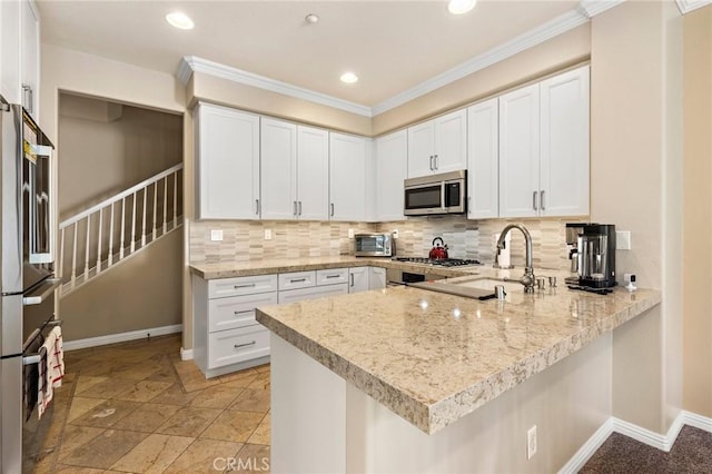 kitchen with tasteful backsplash, appliances with stainless steel finishes, a peninsula, white cabinets, and baseboards