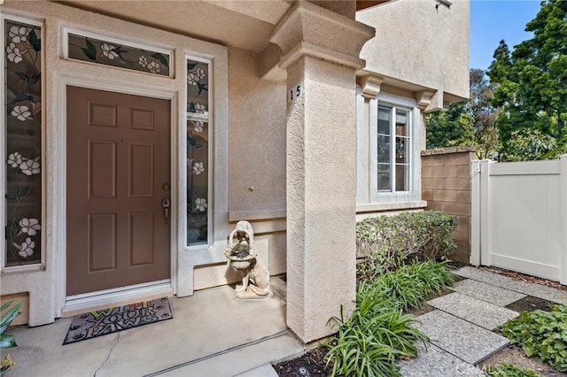 entrance to property featuring stucco siding and fence