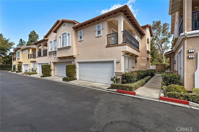 view of front of home with a tiled roof, a garage, a balcony, and stucco siding