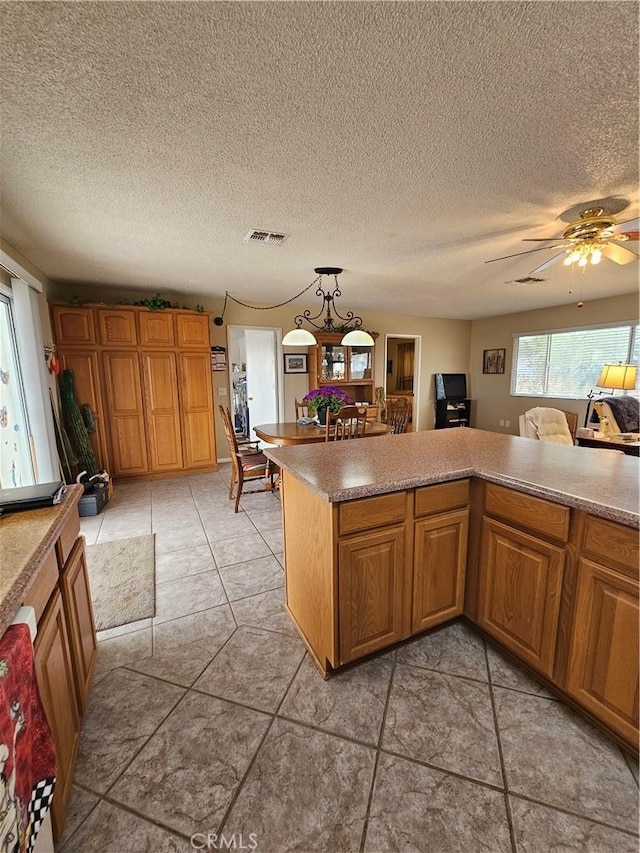 kitchen with ceiling fan, light countertops, visible vents, and brown cabinets