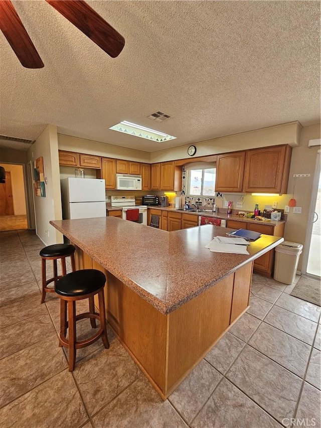 kitchen with a spacious island, visible vents, brown cabinets, and white appliances