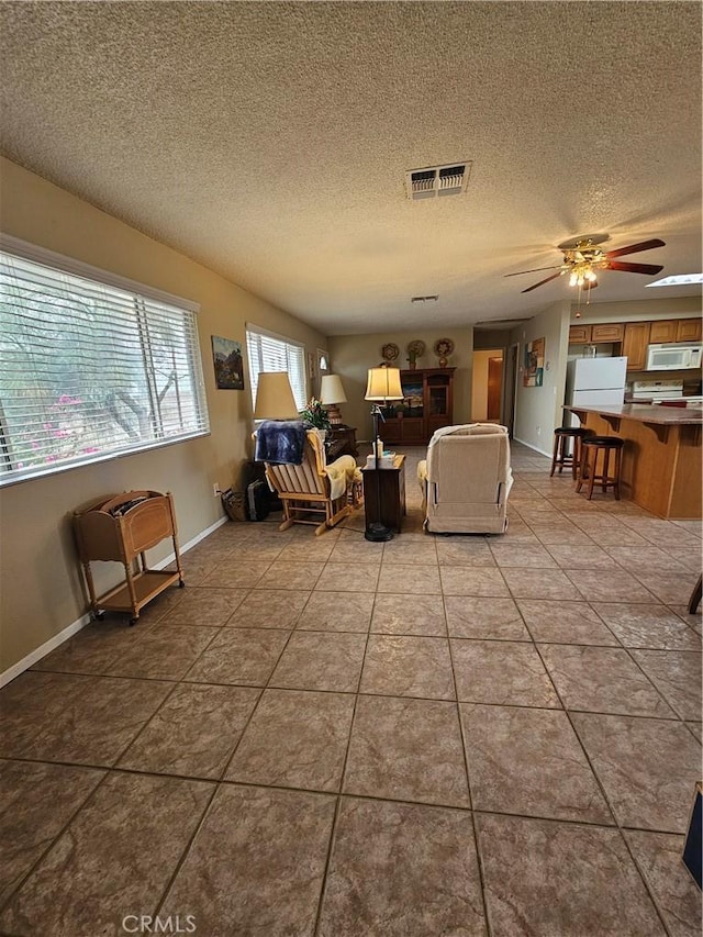 living room featuring visible vents, a textured ceiling, light tile patterned floors, baseboards, and ceiling fan