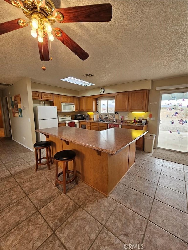 kitchen with a spacious island, ceiling fan, a breakfast bar, brown cabinets, and white appliances