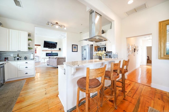 kitchen with visible vents, island exhaust hood, white cabinets, appliances with stainless steel finishes, and backsplash