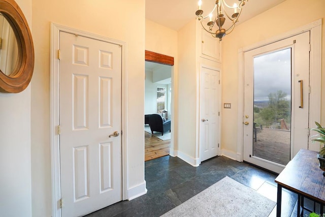 entryway featuring a wealth of natural light, baseboards, stone finish flooring, and an inviting chandelier