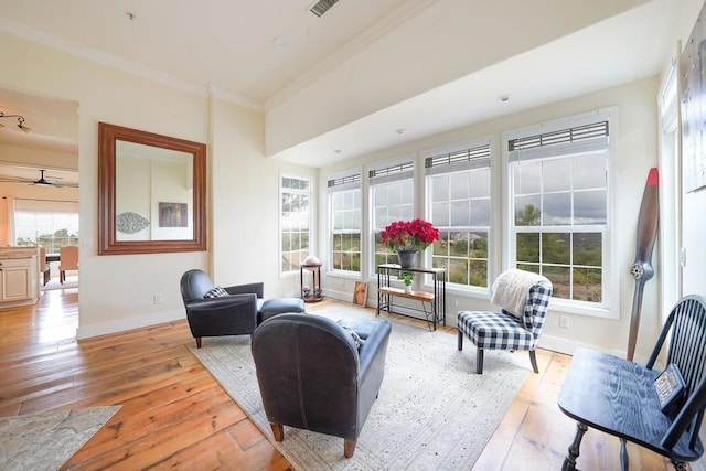 living area featuring baseboards, crown molding, light wood-style floors, and a ceiling fan