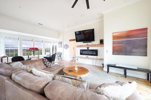 living room featuring visible vents, crown molding, ceiling fan, wood finished floors, and a glass covered fireplace