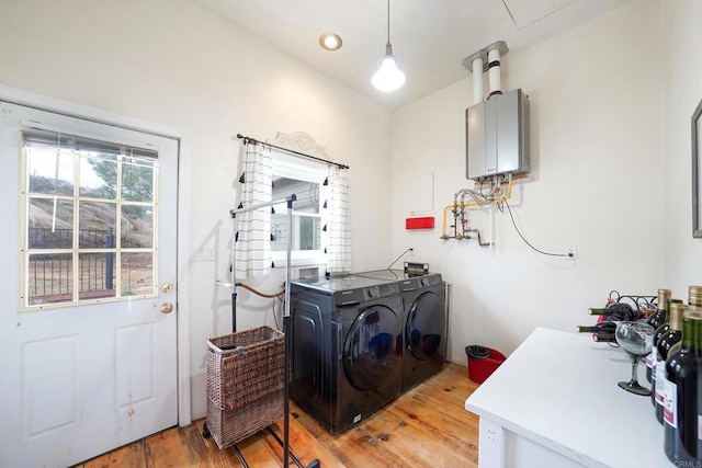 washroom with laundry area, light wood-type flooring, water heater, and washer and clothes dryer