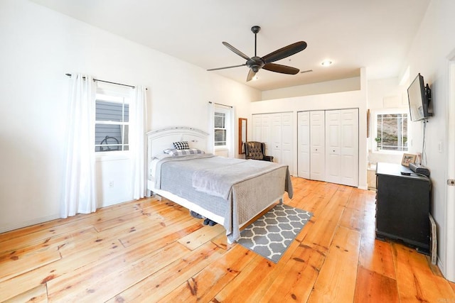 bedroom featuring light wood-type flooring, two closets, and a ceiling fan