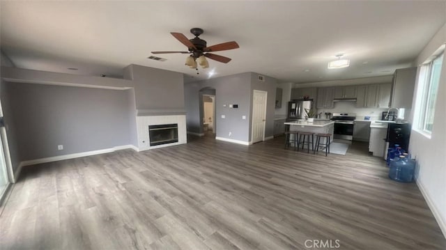 unfurnished living room with visible vents, baseboards, wood finished floors, and a ceiling fan