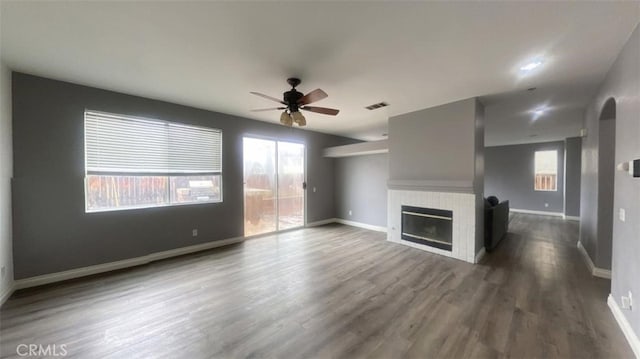 unfurnished living room with baseboards, visible vents, a fireplace, dark wood-style flooring, and ceiling fan