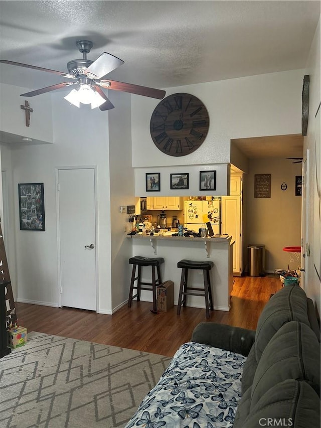 living room featuring baseboards, a textured ceiling, wood finished floors, and a ceiling fan