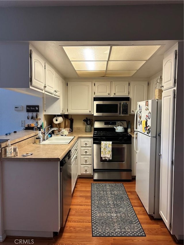 kitchen featuring a sink, stainless steel appliances, light countertops, white cabinetry, and light wood-type flooring