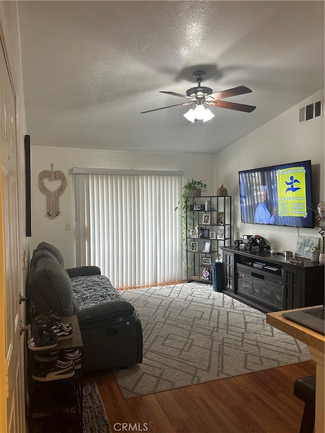 living area featuring wood finished floors, visible vents, ceiling fan, vaulted ceiling, and a textured ceiling