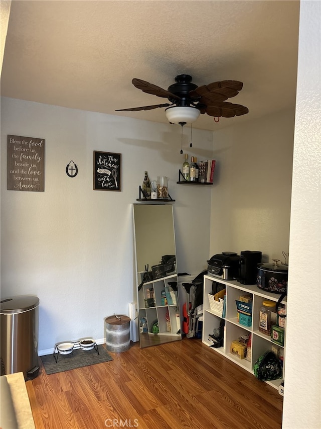 interior space featuring a textured ceiling, baseboards, ceiling fan, and wood finished floors