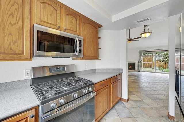 kitchen with visible vents, a lit fireplace, brown cabinetry, stainless steel appliances, and a ceiling fan