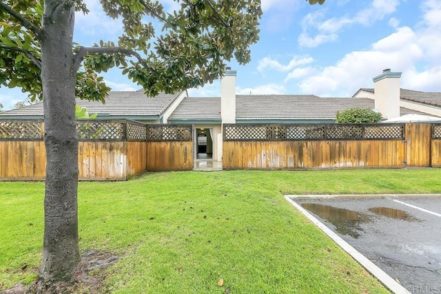 exterior space featuring a lawn, a fenced backyard, a chimney, and a tiled roof