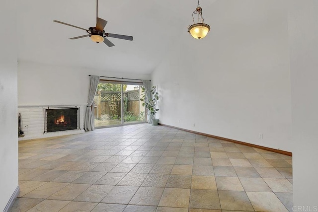 unfurnished living room featuring baseboards, a lit fireplace, a towering ceiling, and a ceiling fan