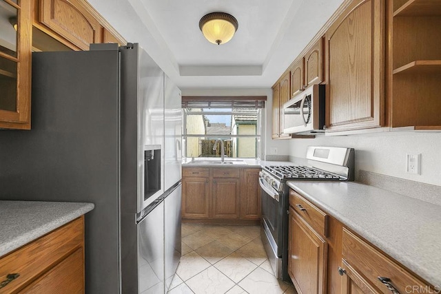 kitchen featuring a sink, a tray ceiling, open shelves, appliances with stainless steel finishes, and brown cabinetry