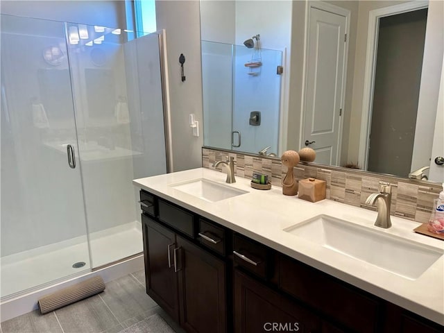 full bath featuring decorative backsplash, double vanity, a stall shower, and a sink