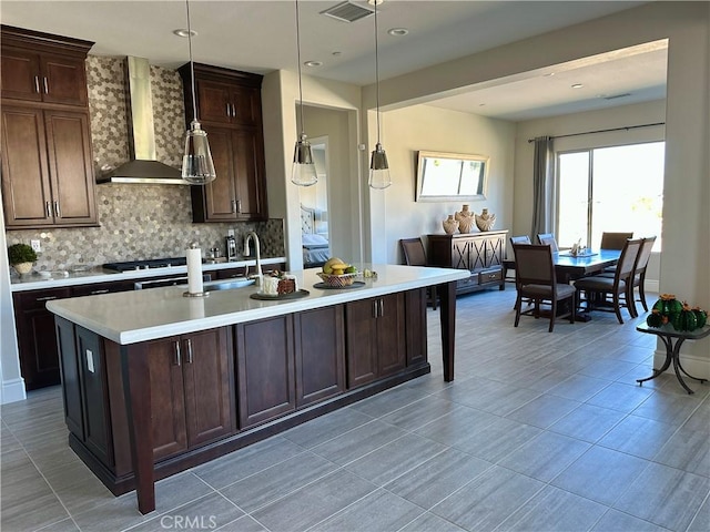 kitchen featuring visible vents, a sink, tasteful backsplash, wall chimney exhaust hood, and light countertops