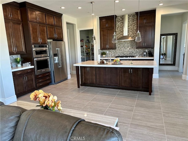 kitchen featuring open floor plan, stainless steel appliances, wall chimney exhaust hood, light countertops, and dark brown cabinets