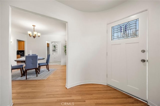 entrance foyer with a notable chandelier, baseboards, and light wood-style floors