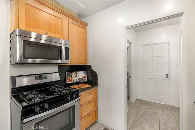 kitchen with dark countertops, light tile patterned floors, appliances with stainless steel finishes, and light brown cabinetry