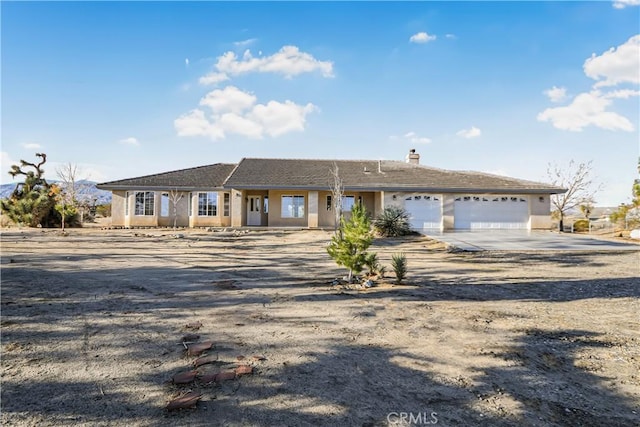 ranch-style home with stucco siding, an attached garage, a chimney, and driveway