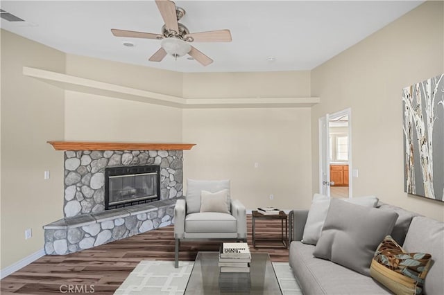 living room with visible vents, a ceiling fan, wood finished floors, a stone fireplace, and baseboards